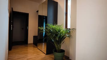 A hallway with wooden flooring, a potted plant, a large mirror, and a door.