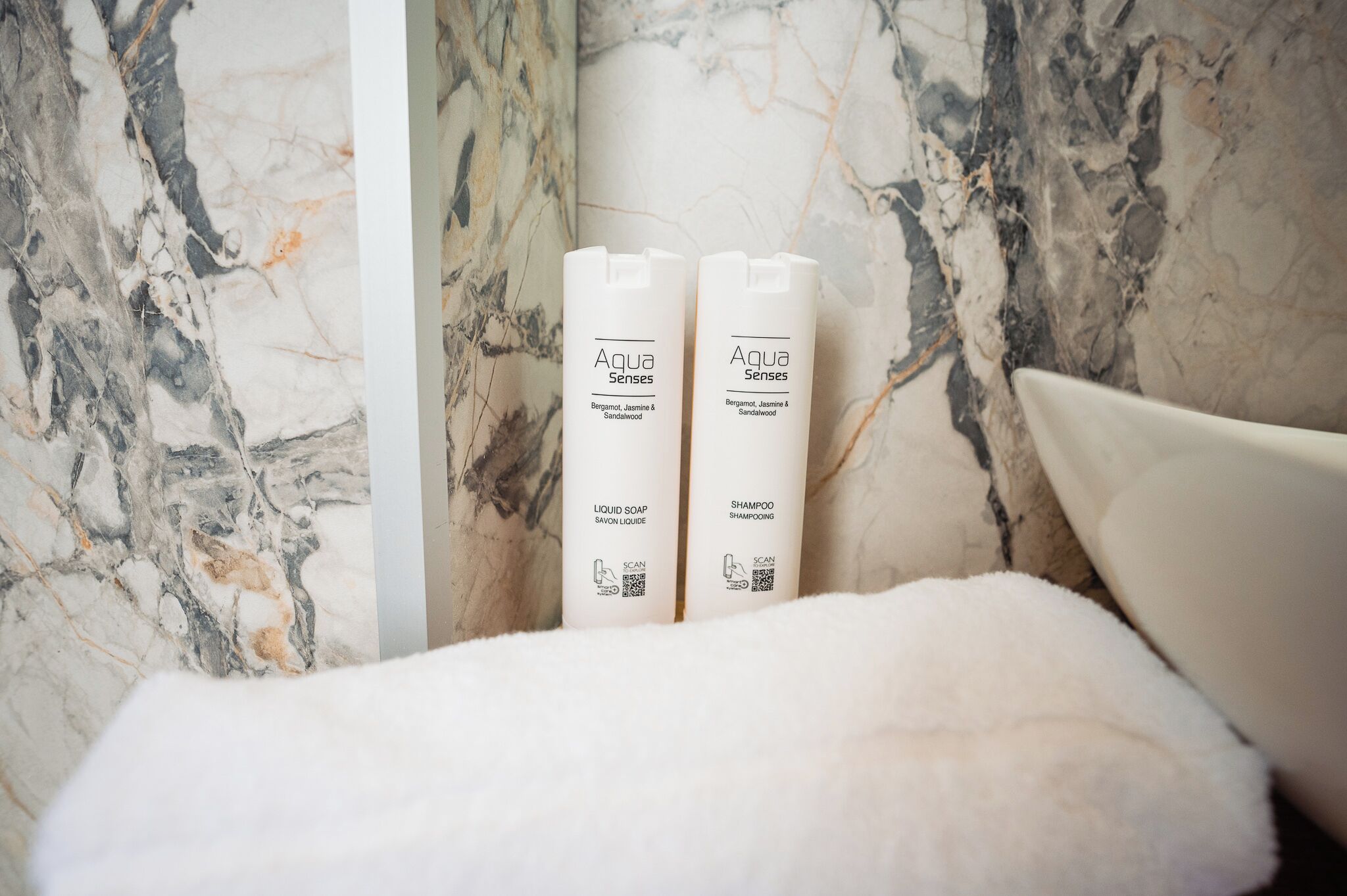Two bottles of Aqua Senses liquid soap and shampoo placed on a white fluffy surface against a marble wall.
