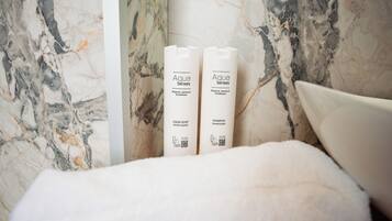 Two bottles of Aqua Senses liquid soap and shampoo placed on a white fluffy surface against a marble wall.