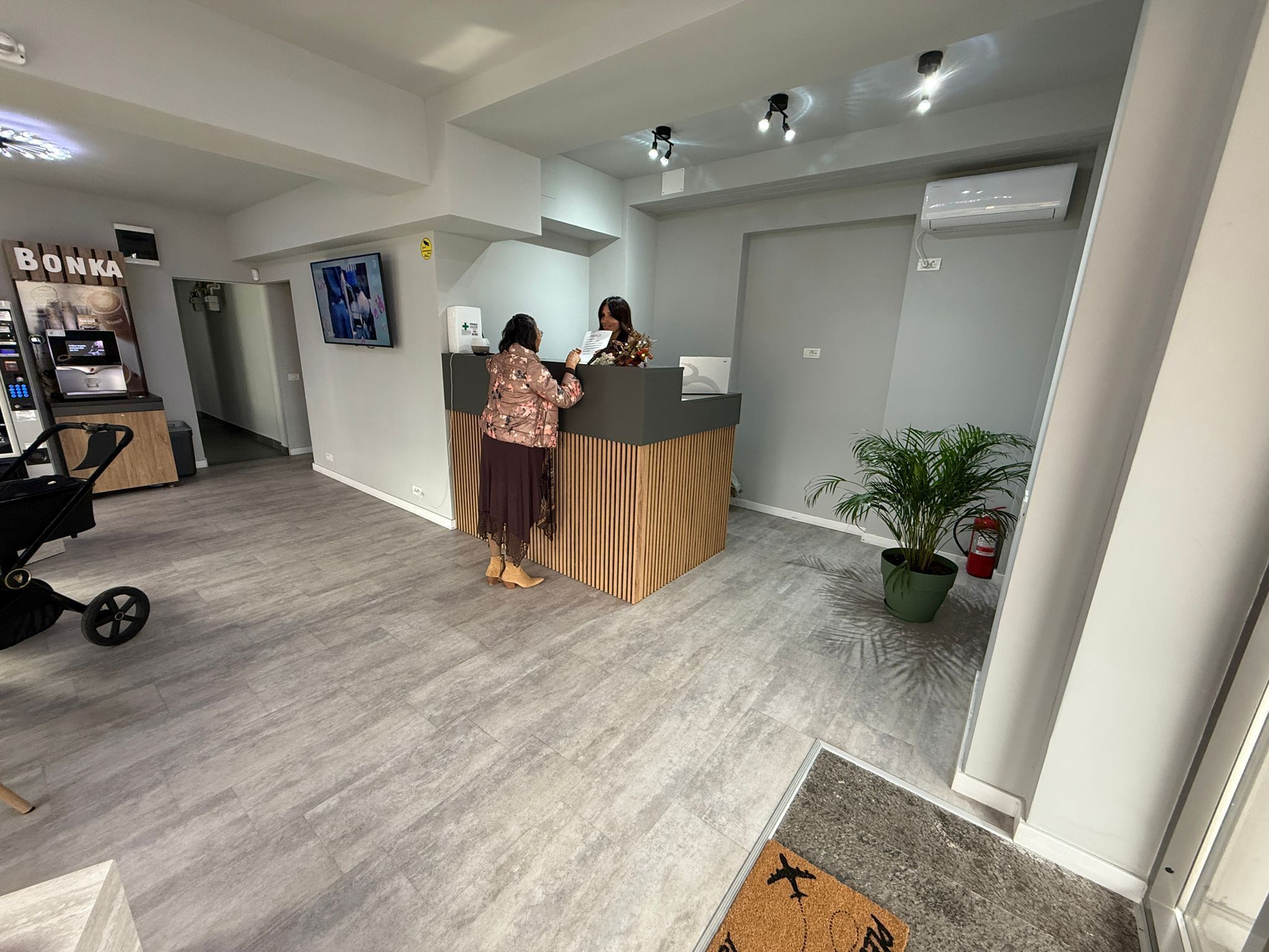 Un espace d’accueil avec un comptoir de réception en bois, un téléviseur fixé au mur et une plante en pot.