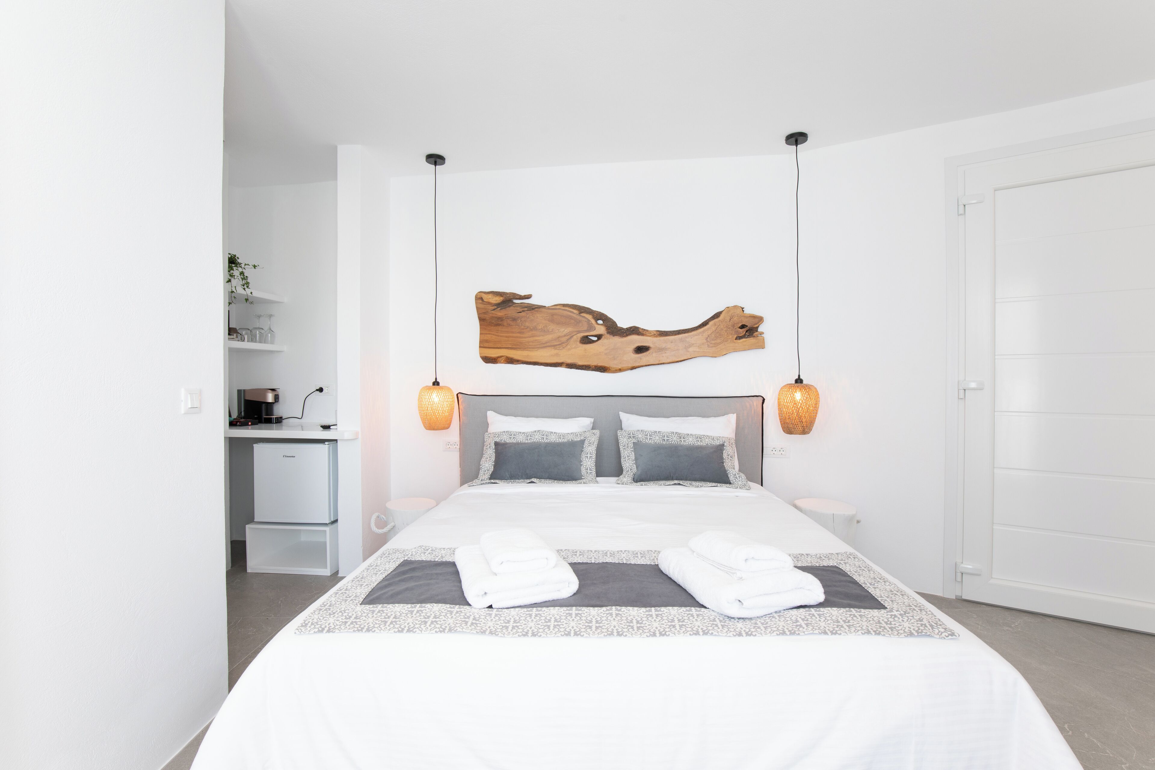 Une chambre d’hôtel moderne avec un grand lit, une œuvre d’art en bois au-dessus du lit, un petit bureau avec une lampe et une armoire blanche.