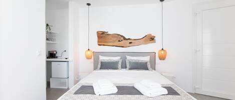 Une chambre d’hôtel moderne avec un grand lit, une œuvre d’art en bois au-dessus du lit, un petit bureau avec une lampe et une armoire blanche.