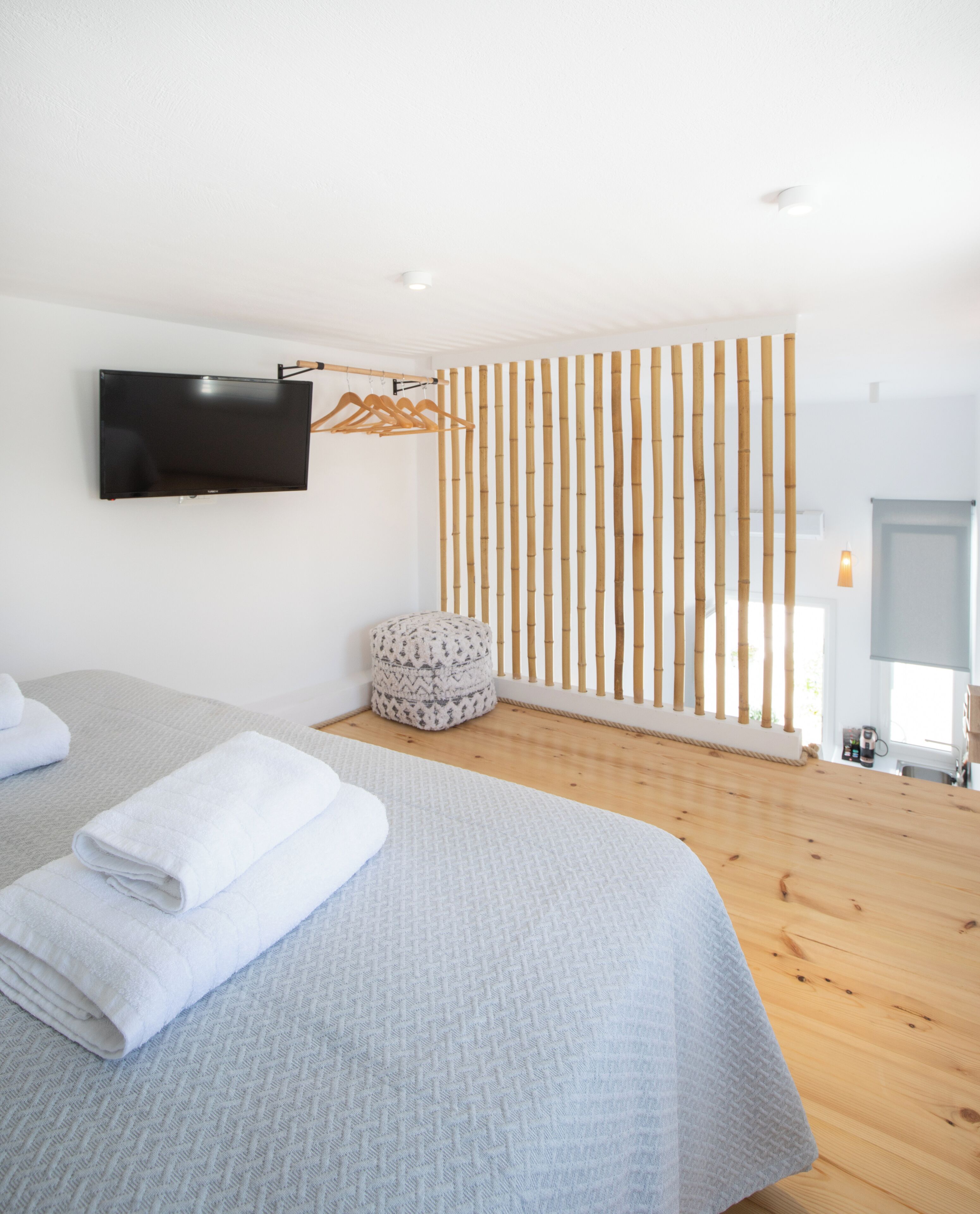 A modern bedroom with a large bed, a flat-screen TV, a wooden floor, and a bamboo partition.