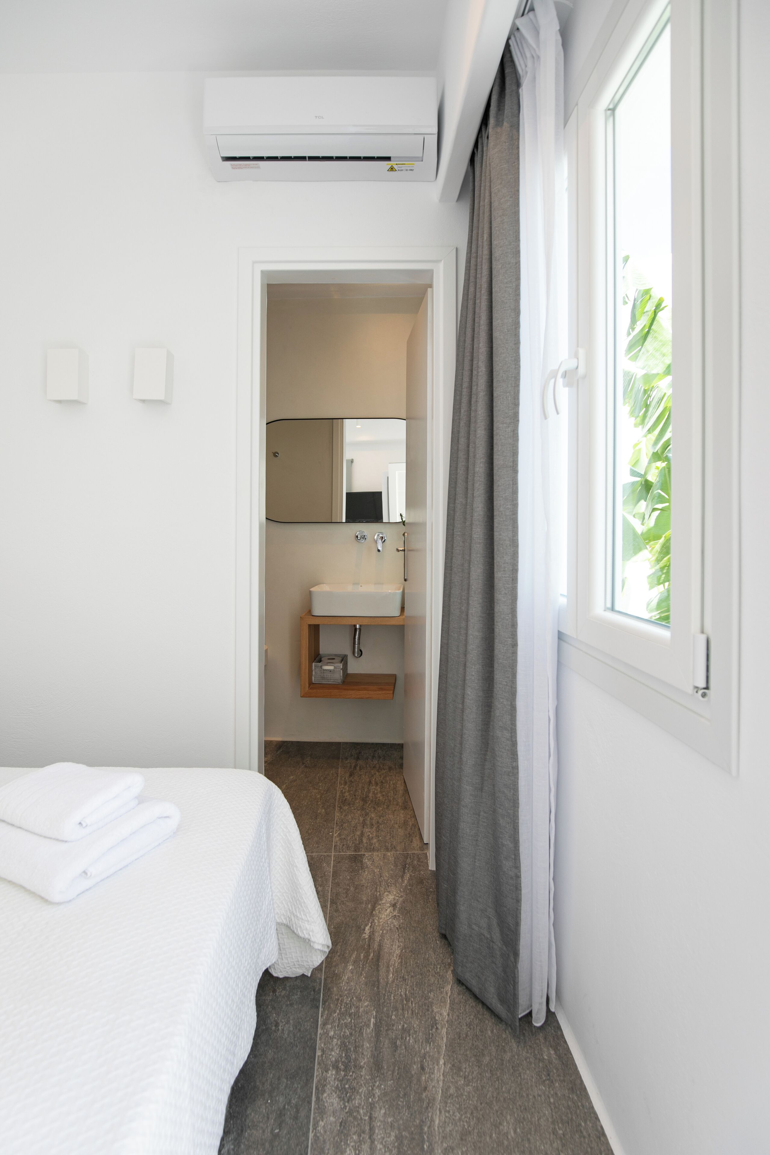 A hotel room with a bed, a bathroom with a sink and mirror, and a window with curtains.