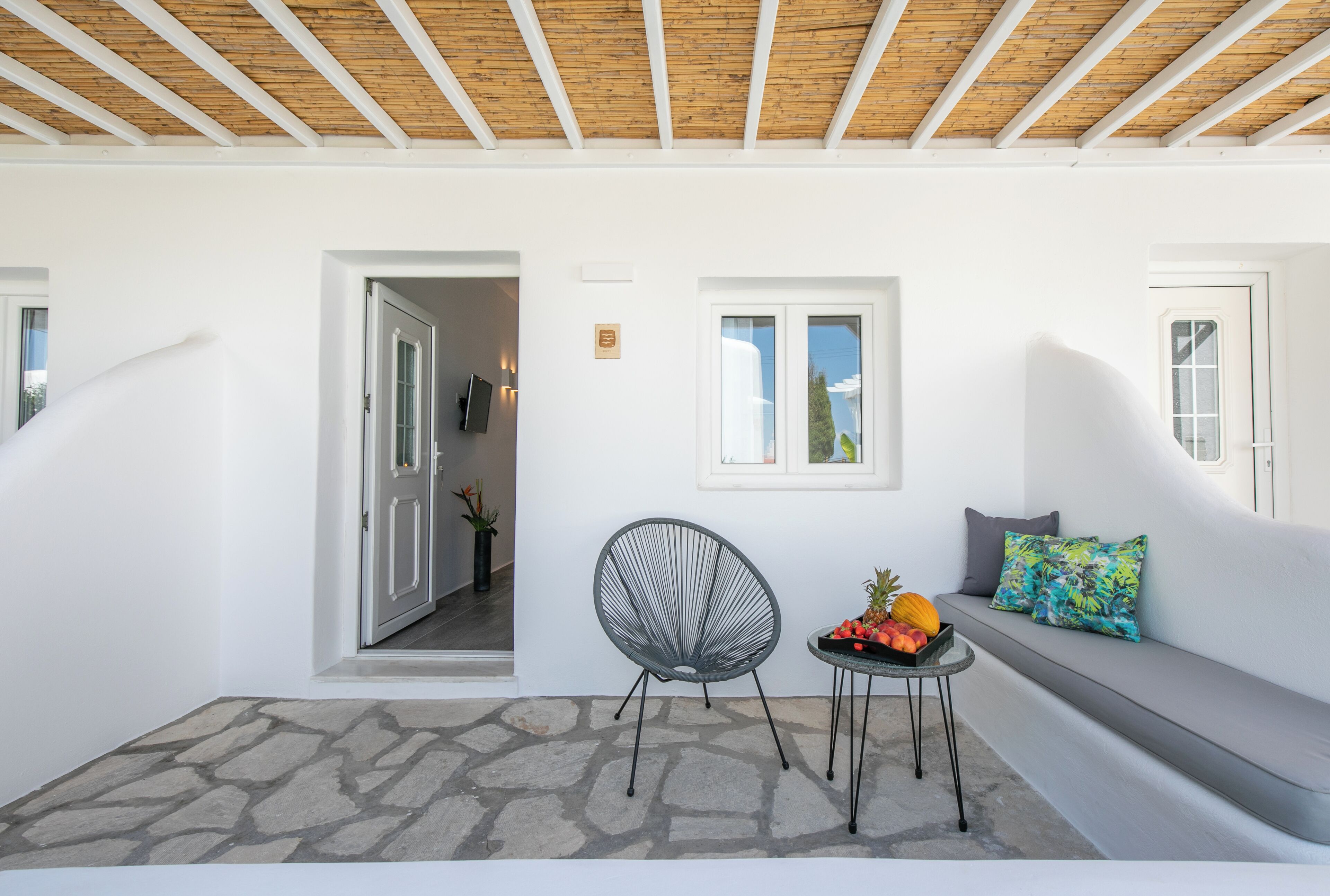 Ein modernes Interieur mit Steinböden, einem runden Sessel, einem kleinen Tisch mit Obst und einer Couch mit bunten Kissen.
