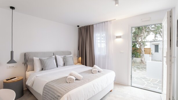 Ein modernes Schlafzimmer mit einem großen Bett, einem Nachttisch, einer Lampe und Blick ins Freie.