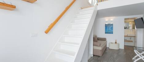 Un intérieur moderne avec un escalier blanc, un canapé et un téléviseur à écran plat.