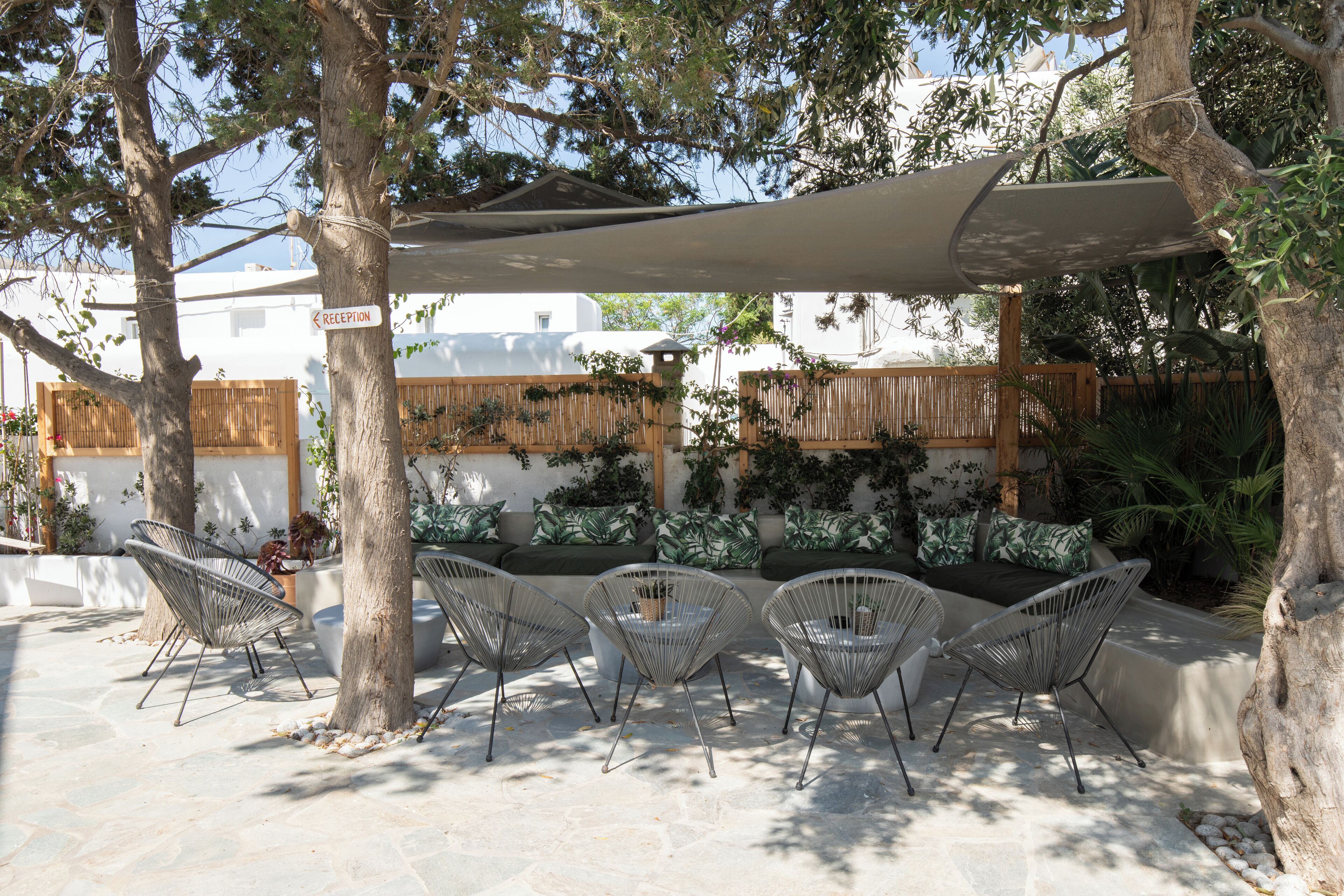 An outdoor seating area with three chairs and a table under a canopy, surrounded by trees and a wooden fence.