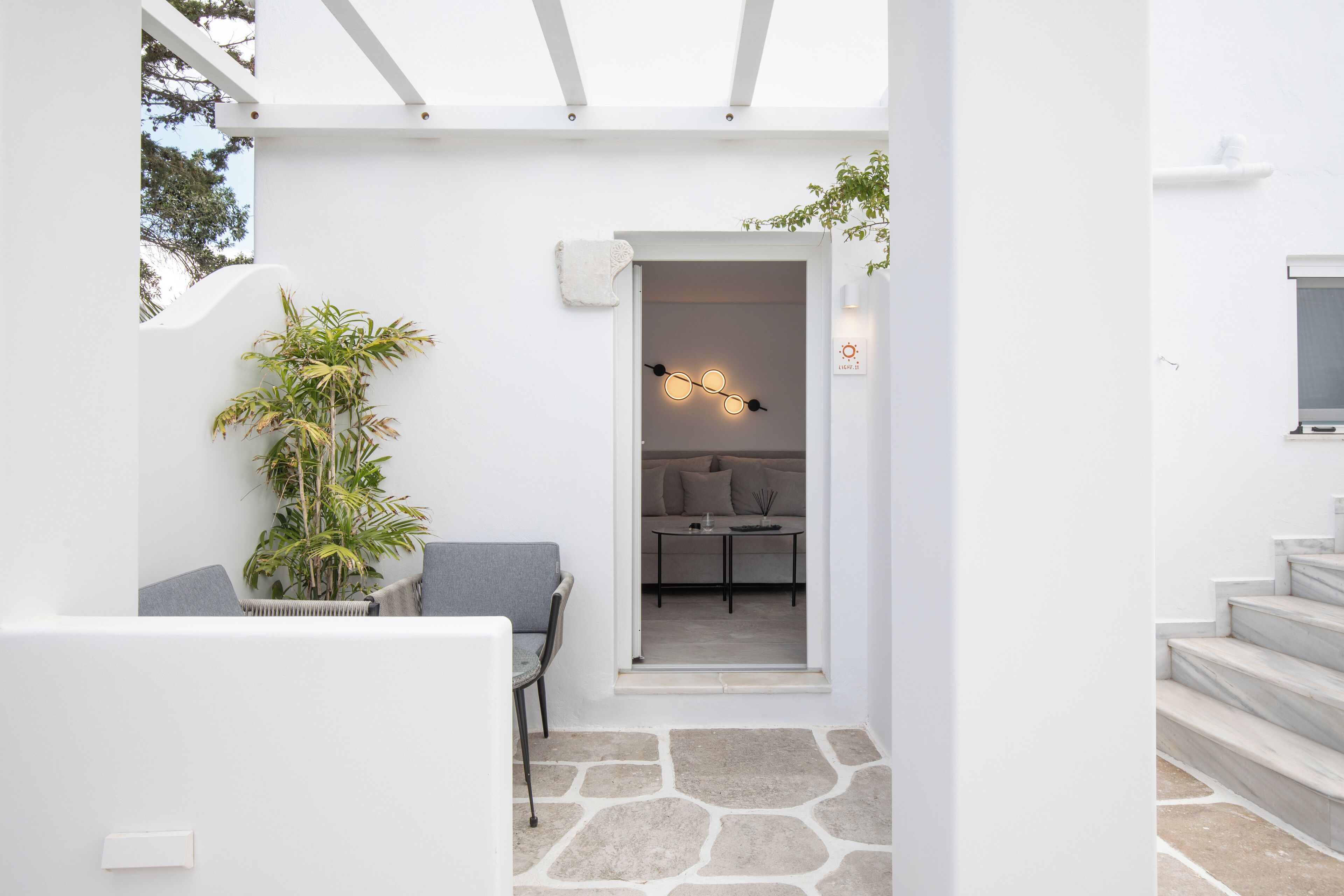 Un interior moderno y minimalista con suelo de piedra, una zona de estar con una planta y un rincón acogedor con una mesa y cojines.