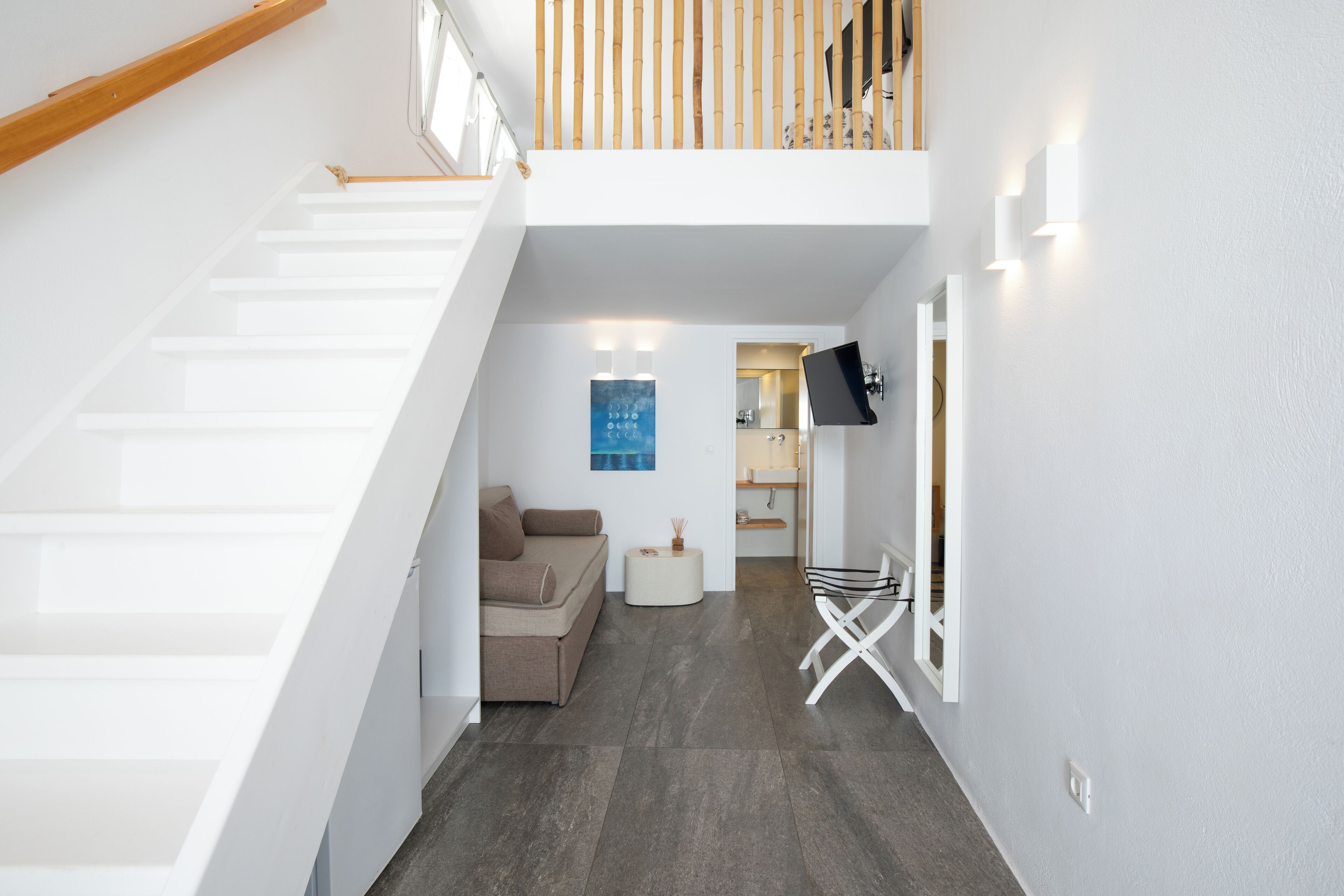 A modern interior with a staircase, a sofa, a small table, and a TV mounted on the wall.