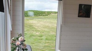 A dining area with a table and chairs, a view of a grassy field through a window, and a gray sofa. - Hotel Studlagil Canyon (Egilsstaðir)