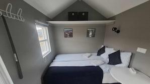 A compact bedroom with a bed, bedside table, and a small window. - Hotel Studlagil Canyon (Egilsstaðir)