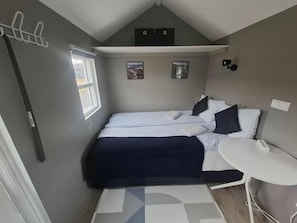 A compact bedroom with a bed, bedside table, and a small window. - Hotel Studlagil Canyon (Egilsstaðir)