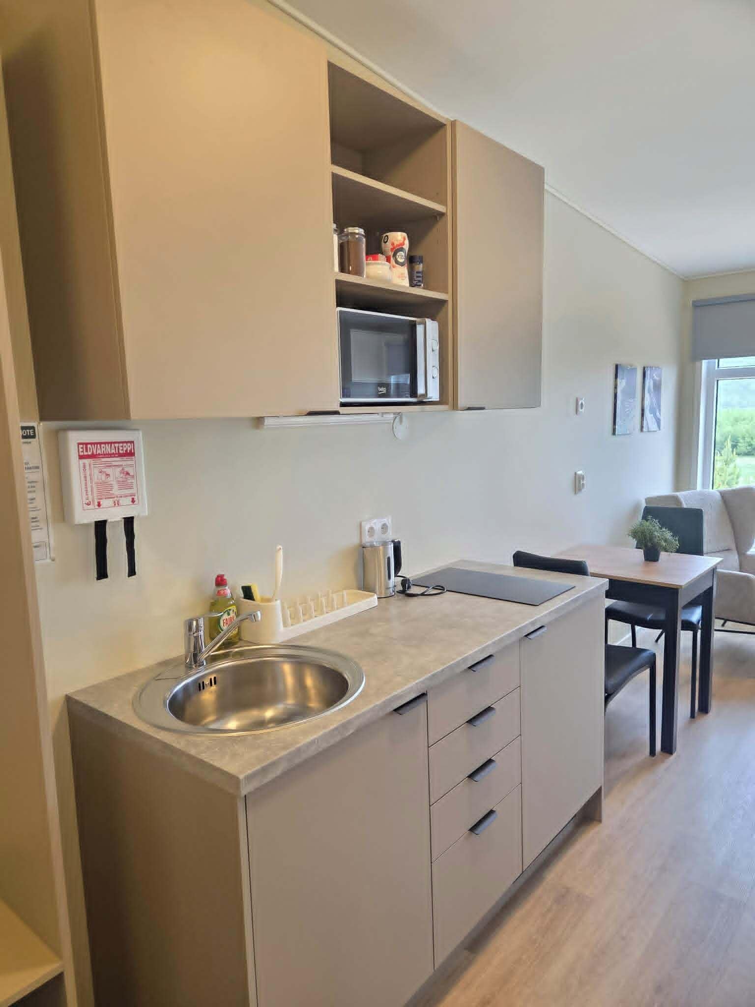 A modern kitchen with a built-in microwave, a stainless steel sink, and a countertop with a bottle of dish soap.