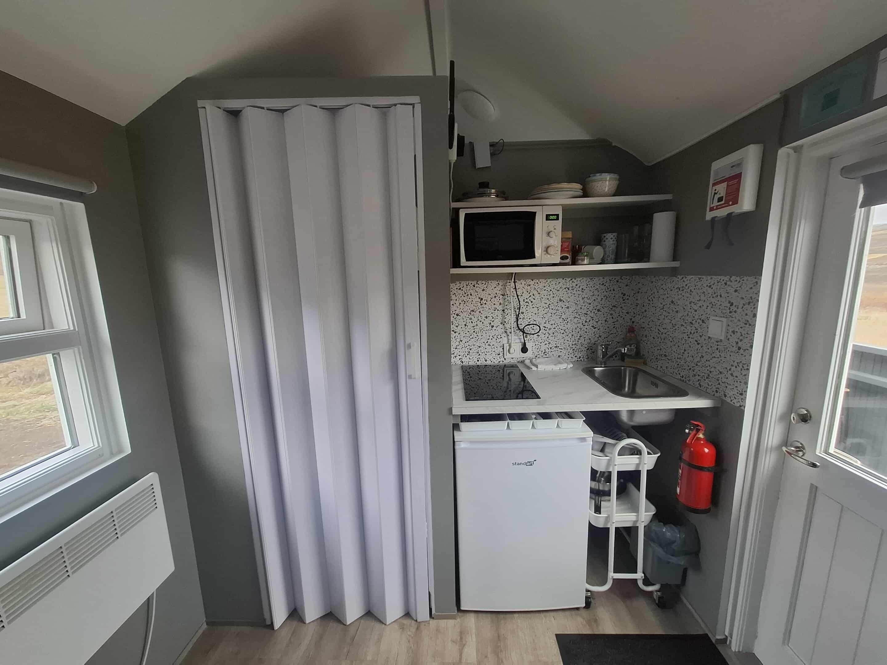Een kleine keuken met een magnetron, spoelbak en een compacte koelkast.