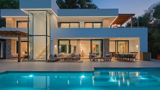 Une maison moderne à deux étages, dotée d’une piscine, d’un espace salon extérieur et d’une façade en pierre.