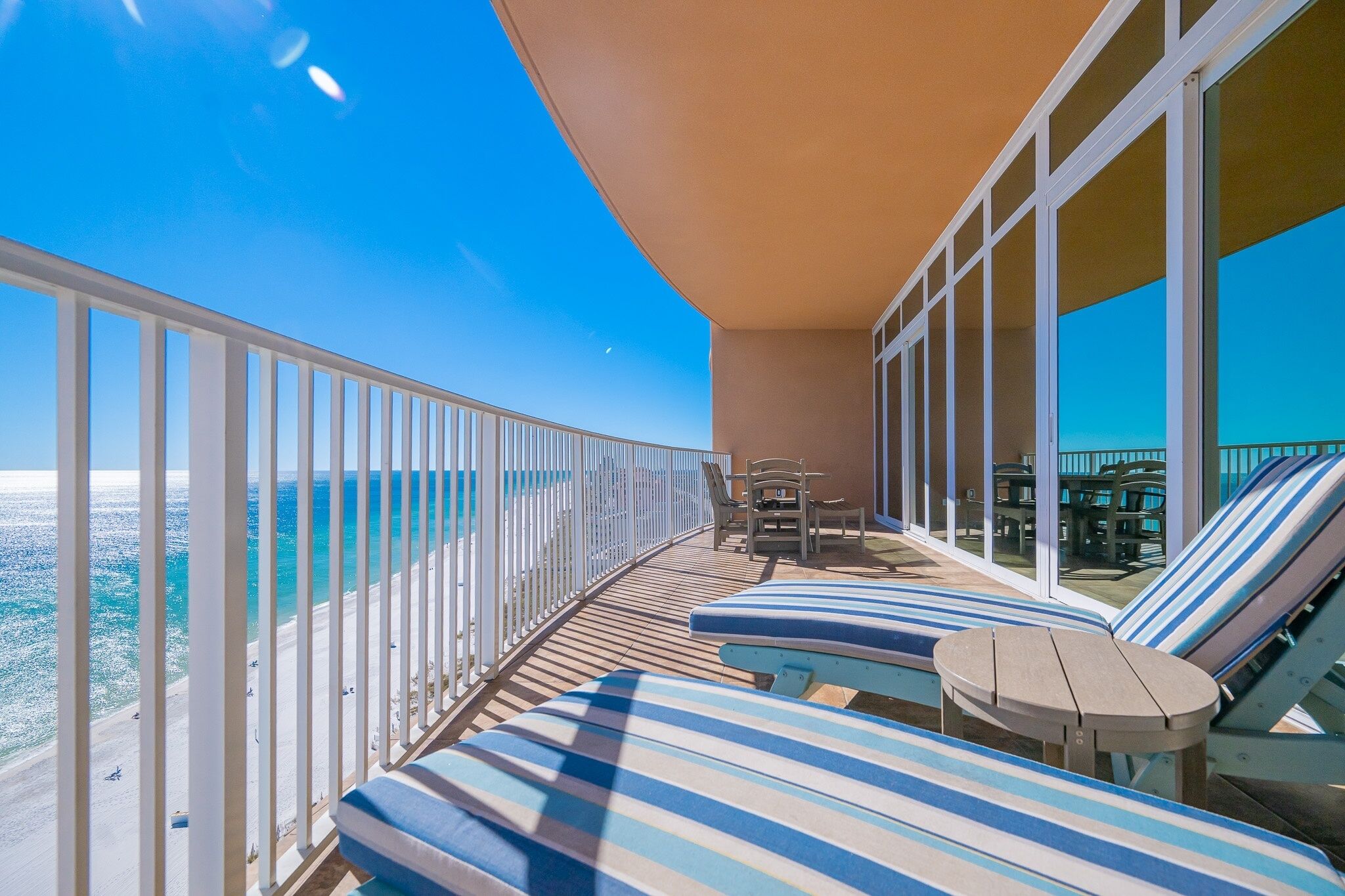 A balcony with striped lounge chairs, a small table, and a view of the ocean.
