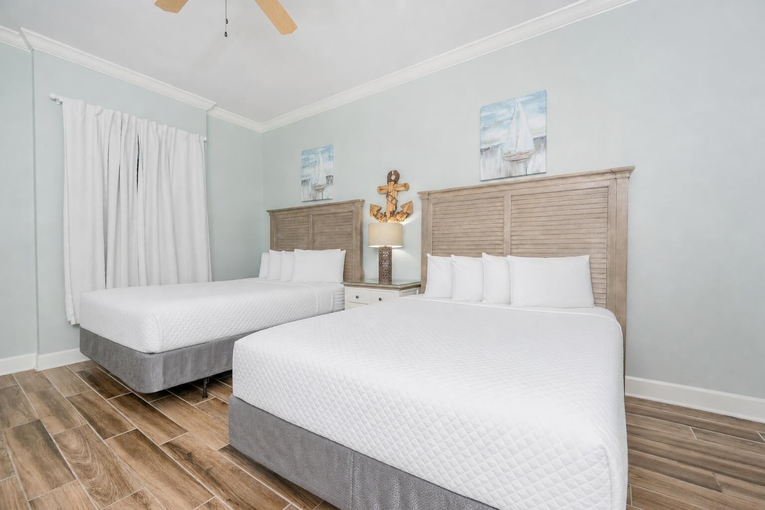 A hotel room with two beds, a wooden headboard, a nightstand with a lamp, and a painting on the wall.