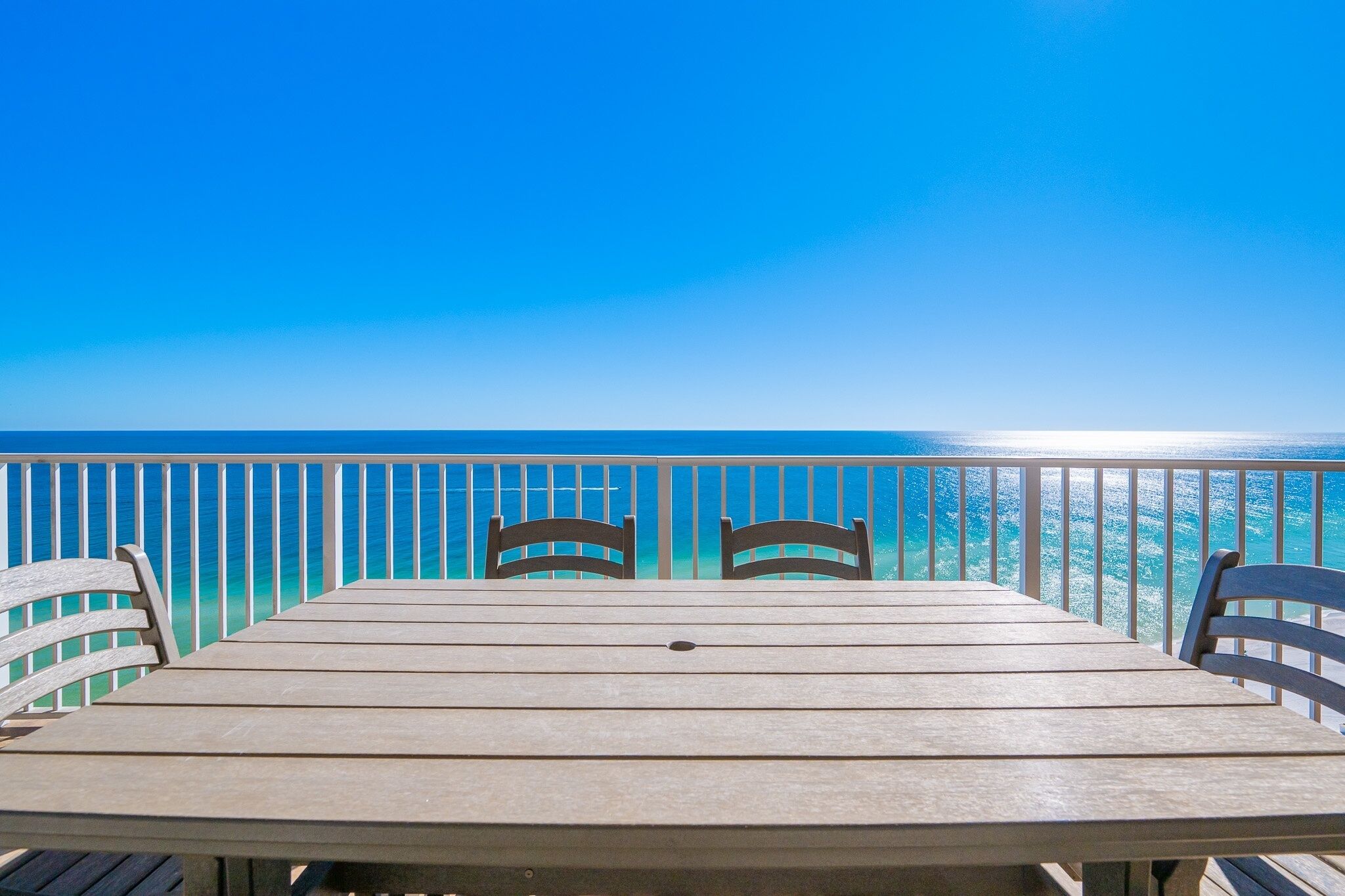 A wooden table with four chairs on a balcony with a view of the ocean.