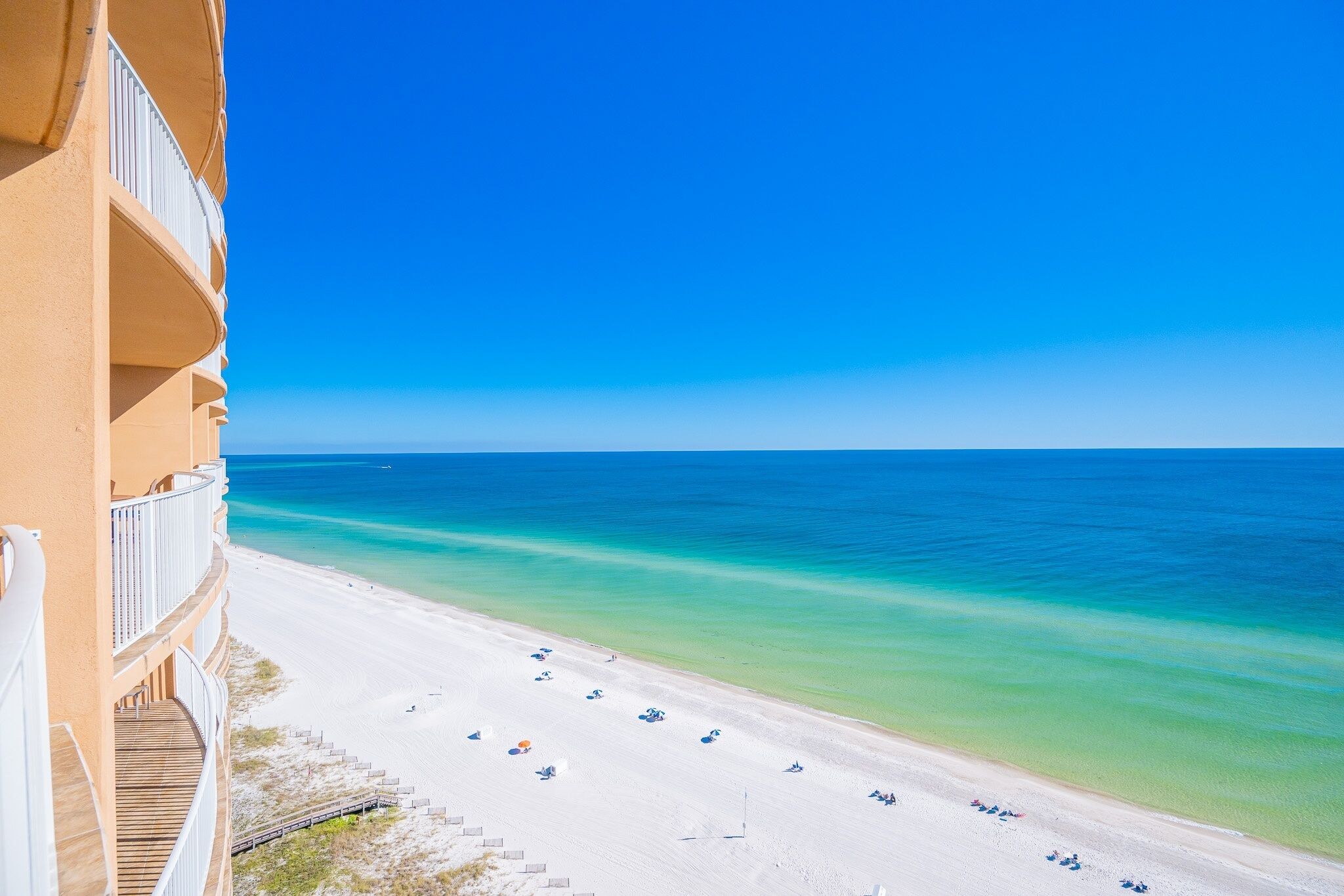 A beachfront hotel with a balcony overlooking a sandy beach and clear blue waters.