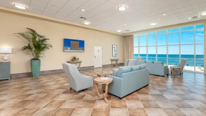 A spacious lobby with a large window offering a view of the ocean, a seating area with sofas and chairs, and a potted plant. - Phoenix Orange Beach 604 3 Bedroom Condo (Orange Beach)