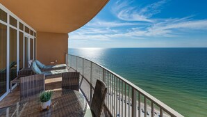 A balcony with wicker furniture, a potted plant, and a view of the ocean.