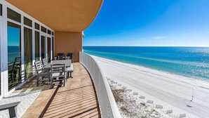 Un balcon doté d’une terrasse en bois, d’une table avec des chaises et offrant une vue sur une plage aux eaux d’un bleu cristallin.