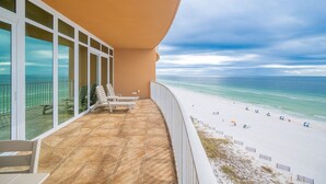 A balcony with a view of the beach, featuring a tiled floor and several chairs.