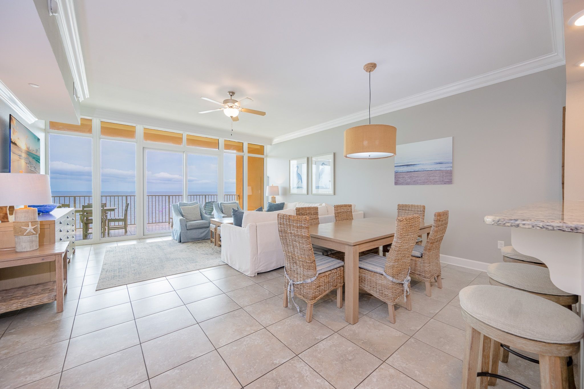 A spacious living area with a large dining table, wicker chairs, and a view of the ocean.
