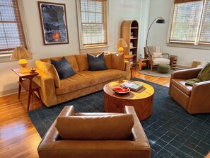 A living room with a sofa, coffee table, and armchair, a bookshelf, and a fireplace. - Fort Benning Family Fun House (Columbus)