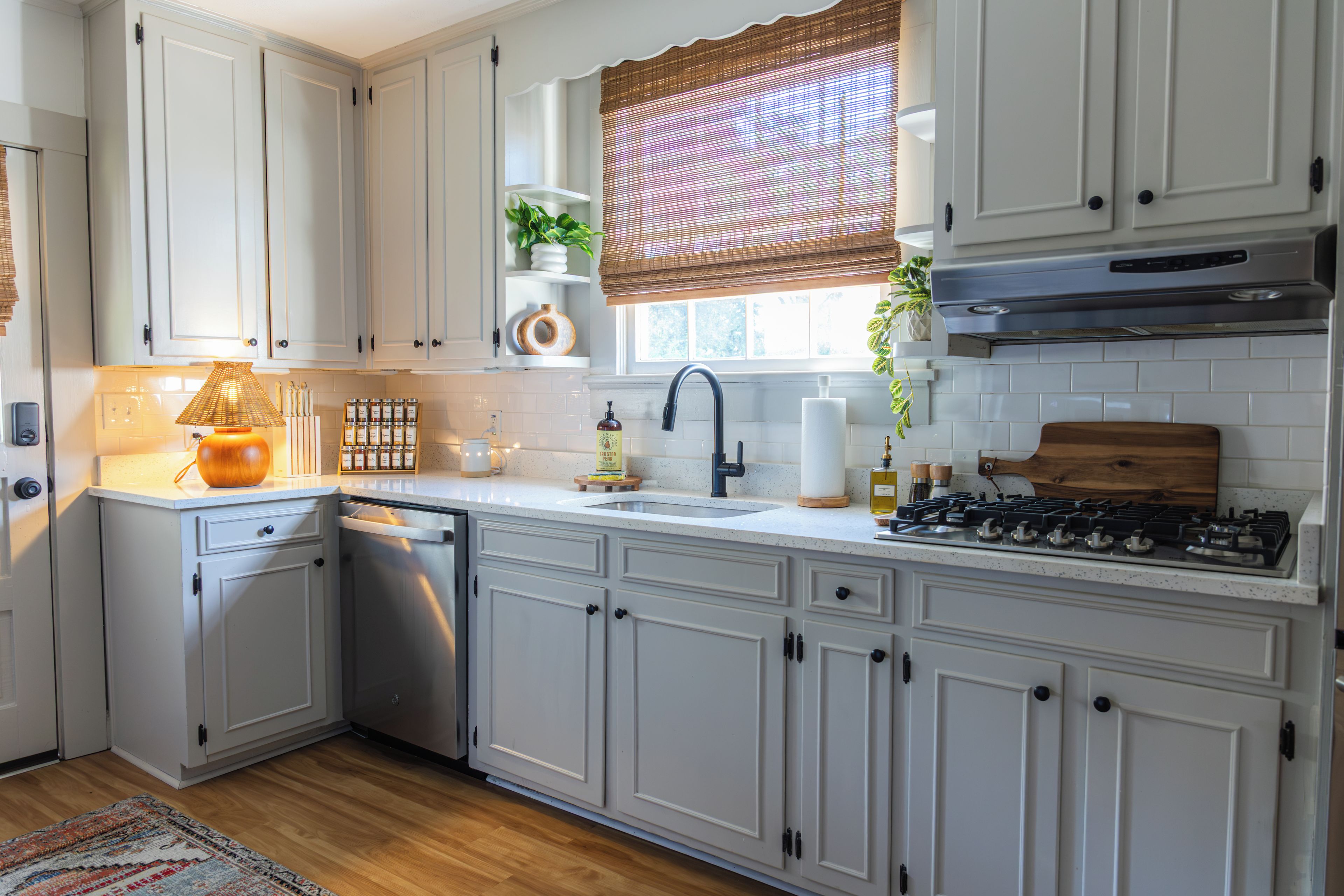 A kitchen with white cabinets, a stove, a sink, and a window with blinds.