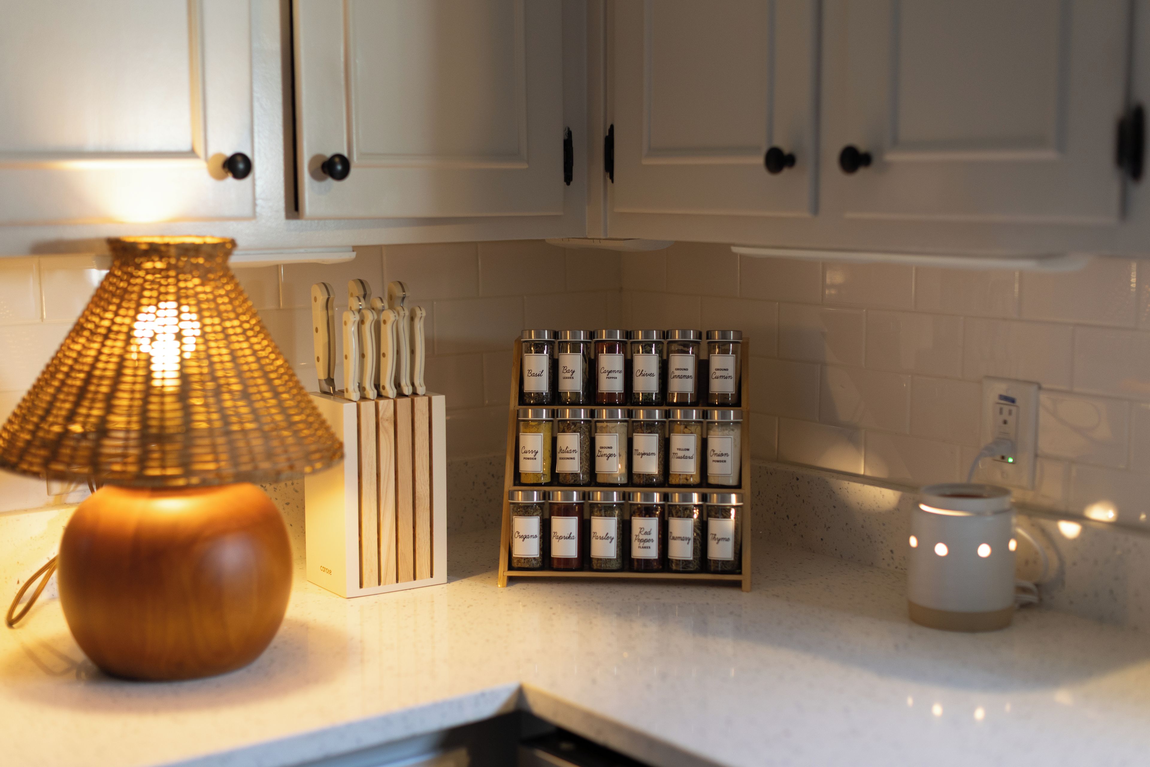A kitchen with a wooden lamp, a spice rack, and a white mug on the counter.