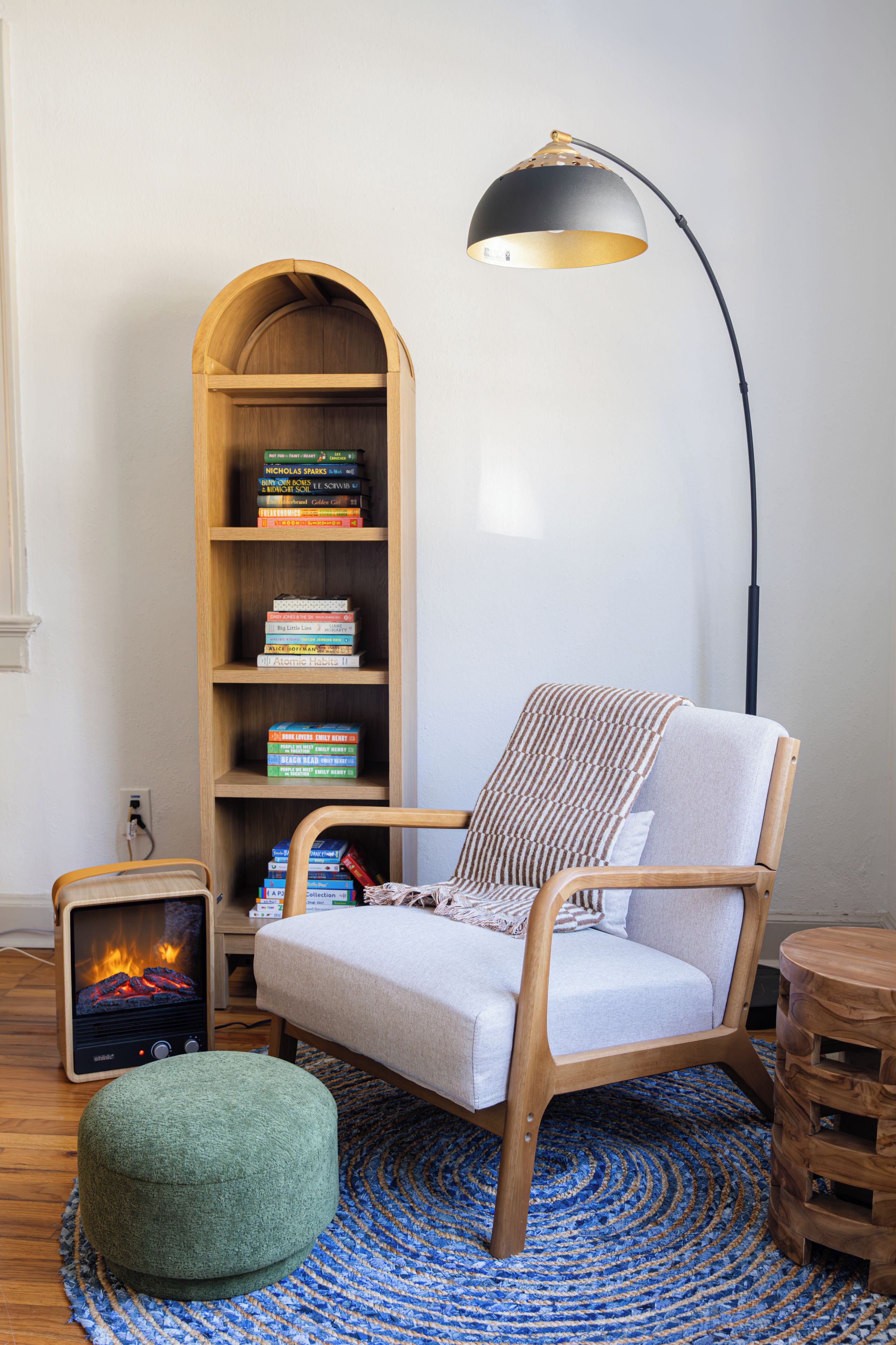 A cozy reading nook with a wooden chair, a small ottoman, a bookshelf, and a fireplace.
