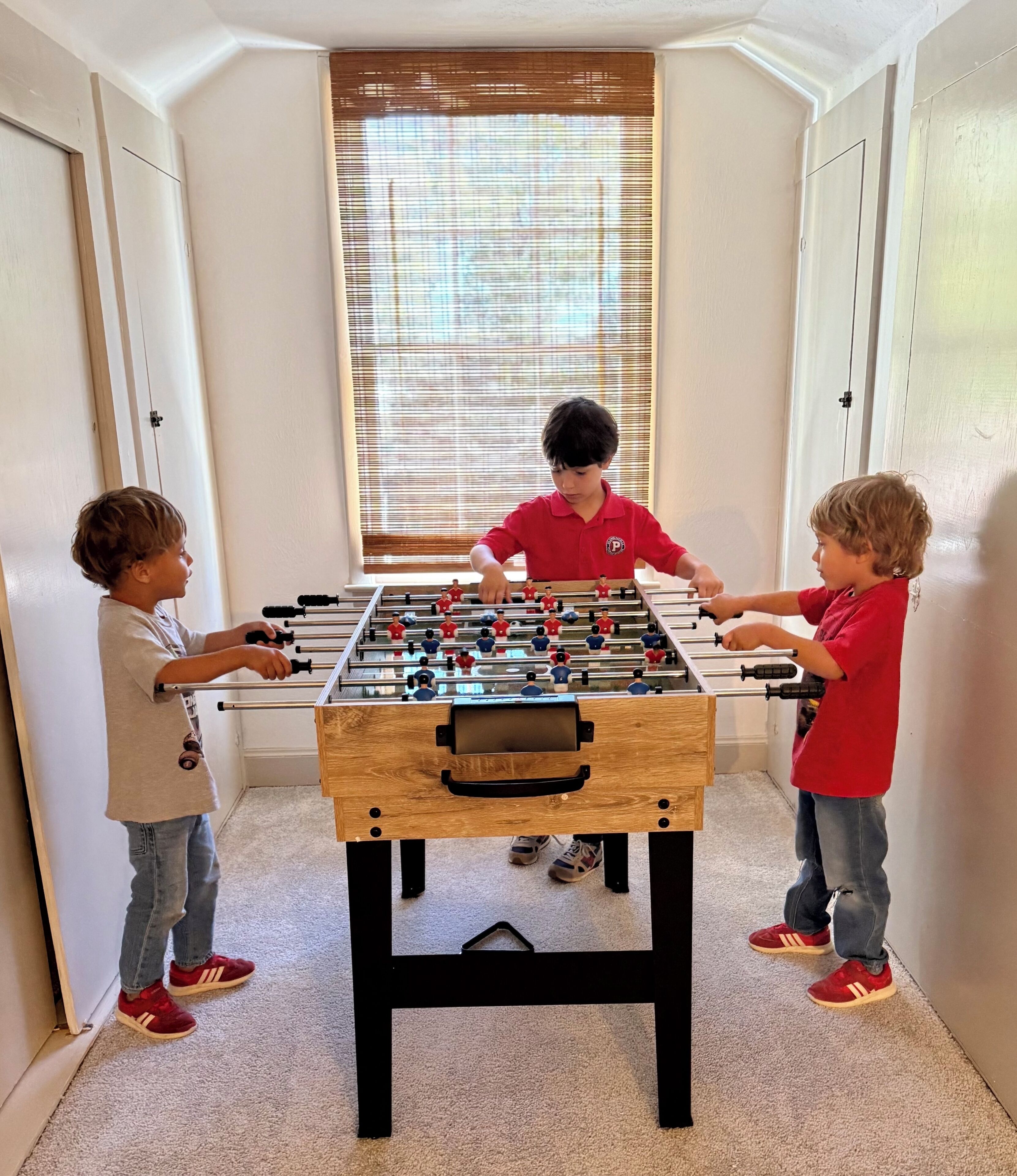 A foosball table in a room with white walls and a window with blinds.