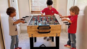 A foosball table in a room with white walls and a window with blinds.