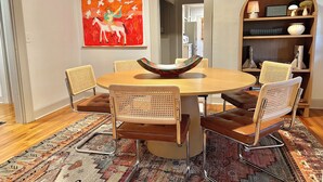 Un coin repas comprenant une table ronde, six chaises, un tapis coloré et une peinture murale.