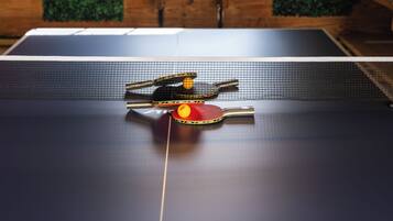 A ping pong table with a ball and paddles, a neon sign reading 'Hideaway', and a window with blinds.