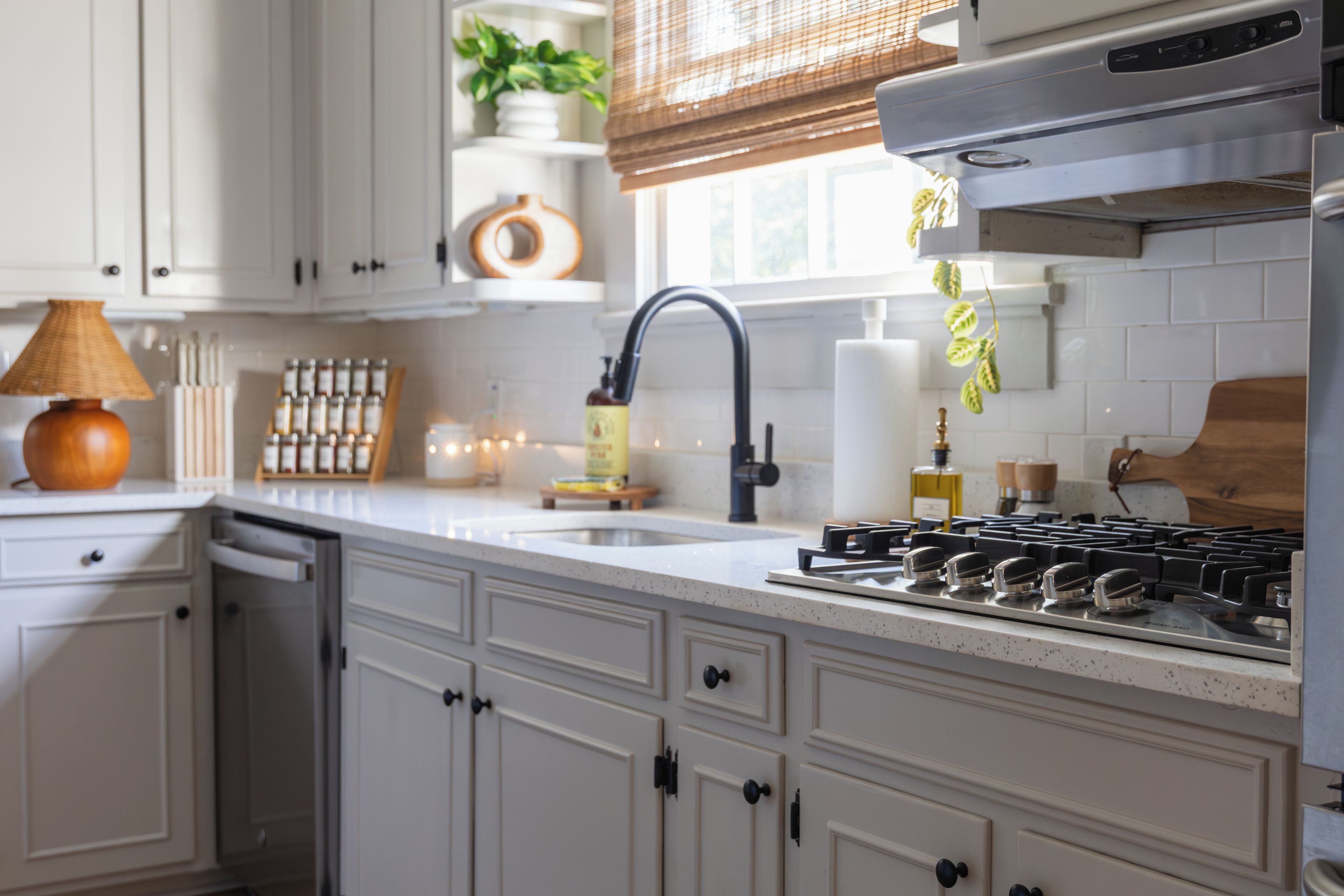A kitchen with white cabinets, a gas stove, a sink, and a window with blinds.