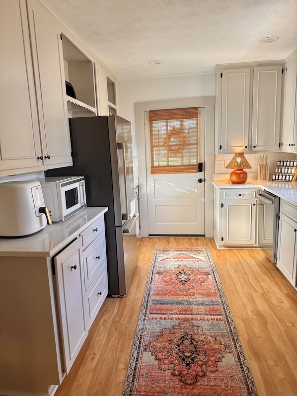 A kitchen with white cabinets, a microwave, a refrigerator, a wooden floor, and a patterned rug.