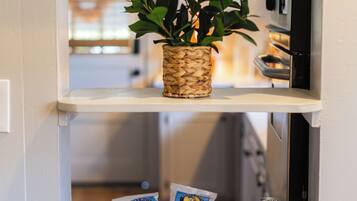 A kitchen shelf with a woven basket containing green plants, a wooden bowl with snacks and a can of soda, and a microwave above.