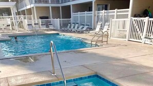 A swimming pool with clear blue water, a metal ladder, and a tiled edge. There are lounge chairs and a white fence in the background. - Across from the beach! Grand Caribbean West 202 (Destin, Florida)
