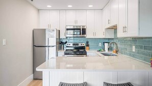 A modern kitchen with white cabinets, stainless steel appliances, a central island, and a blue backsplash. - Across from the beach! Grand Caribbean West 202 (Destin, Florida)