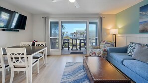 A living room with a TV, a ceiling fan, a sofa, a coffee table, and a dining area with chairs and a table. - Across from the beach! Grand Caribbean West 202 (Destin, Florida)