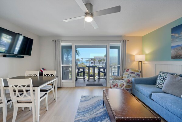 A living room with a TV, a ceiling fan, a sofa, a coffee table, and a dining area with chairs and a table.