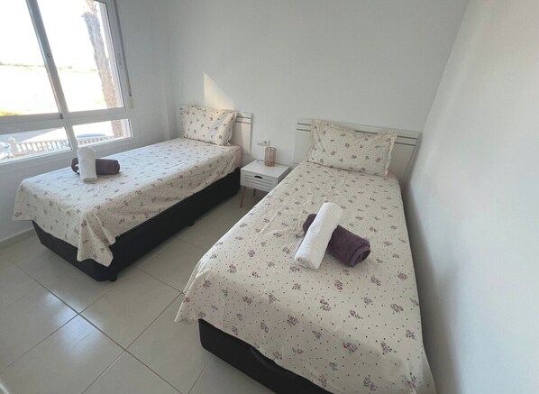 Two single beds with floral bedding, a small bedside table, and a window with a view.
