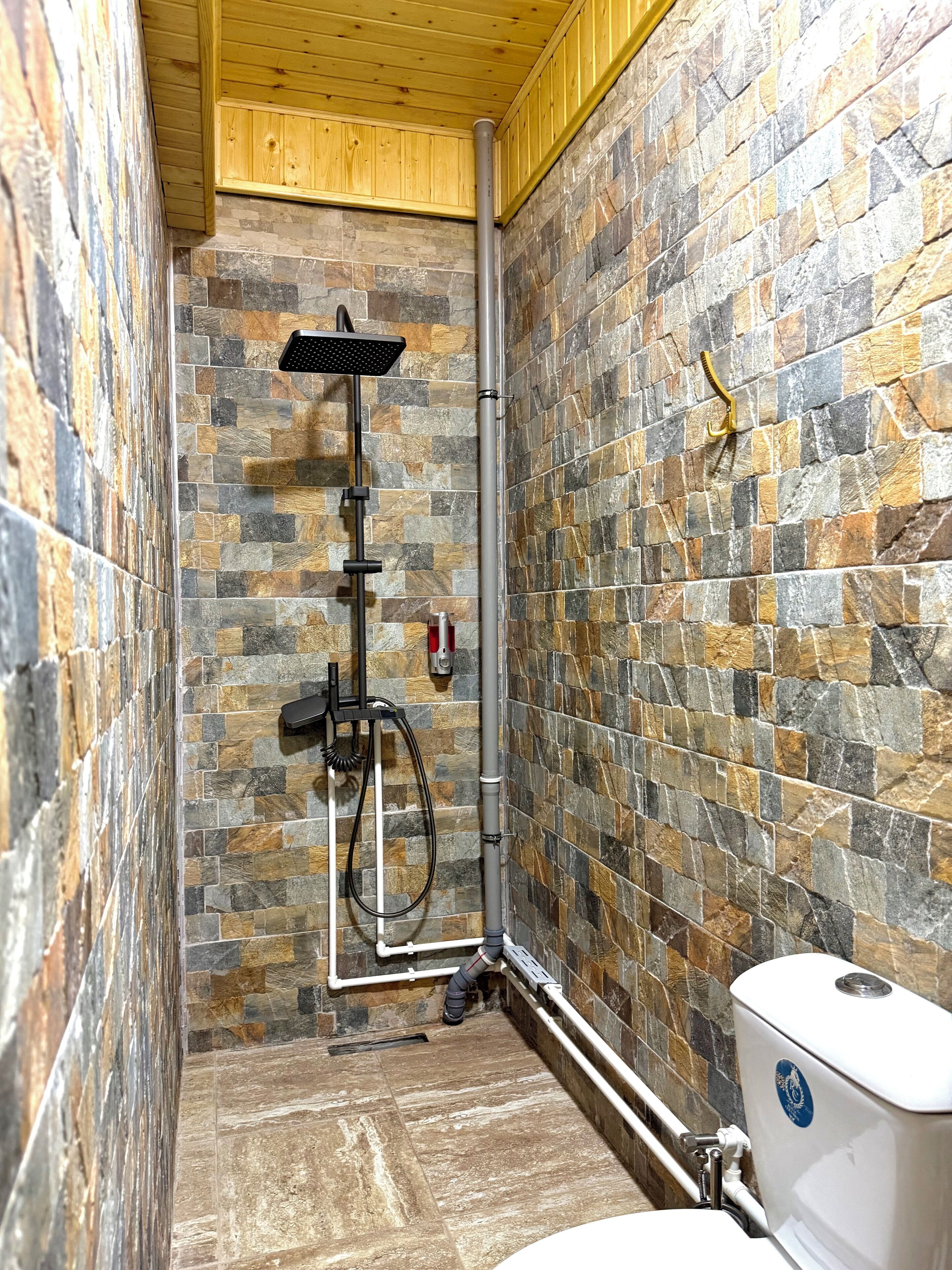 A bathroom with a stone wall, a shower, and a toilet.