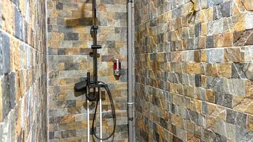 A bathroom with a stone wall, a shower, and a toilet.