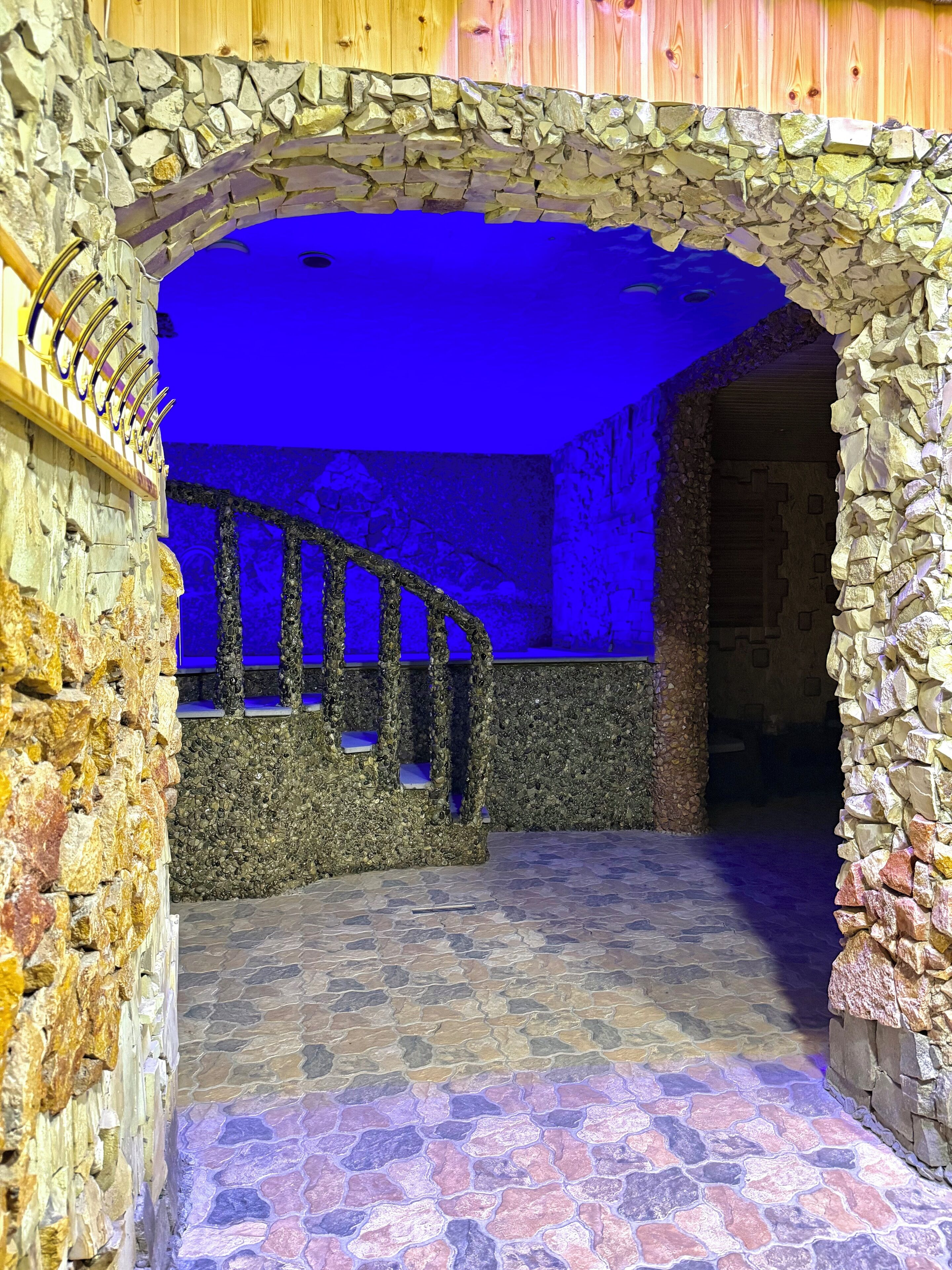 A stone archway leading to a room with a blue-lit interior and a staircase.