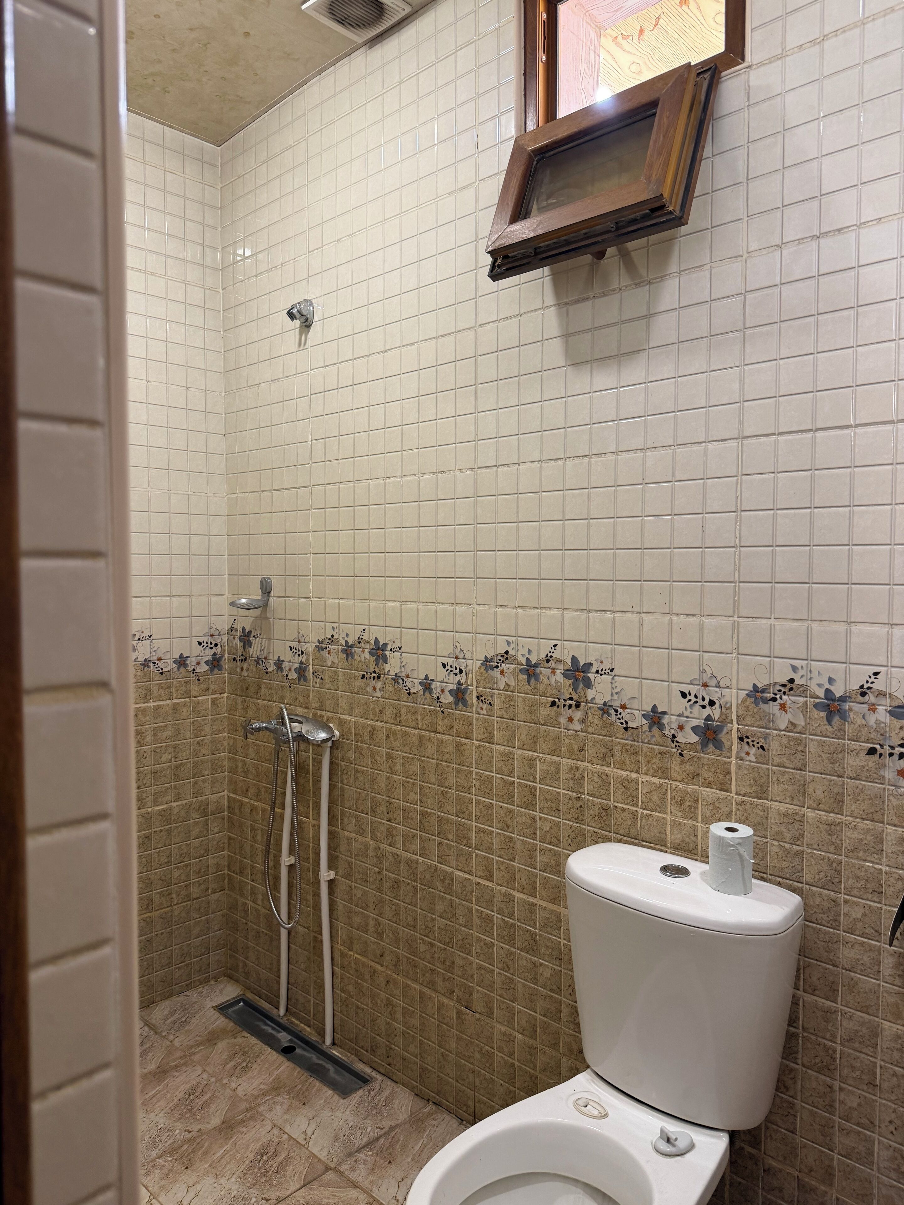 A bathroom with a shower, toilet, and a small window.