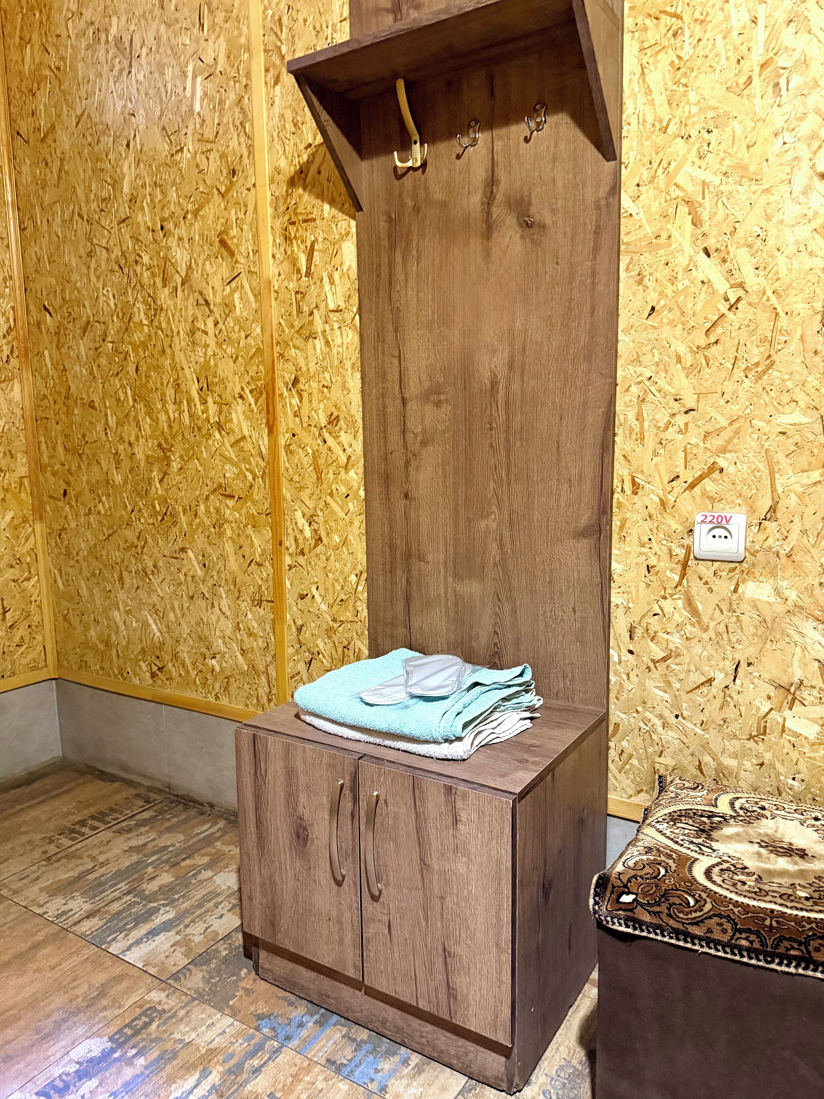 A wooden cabinet with a towel and a small shelf, a wall socket, and a patterned rug.